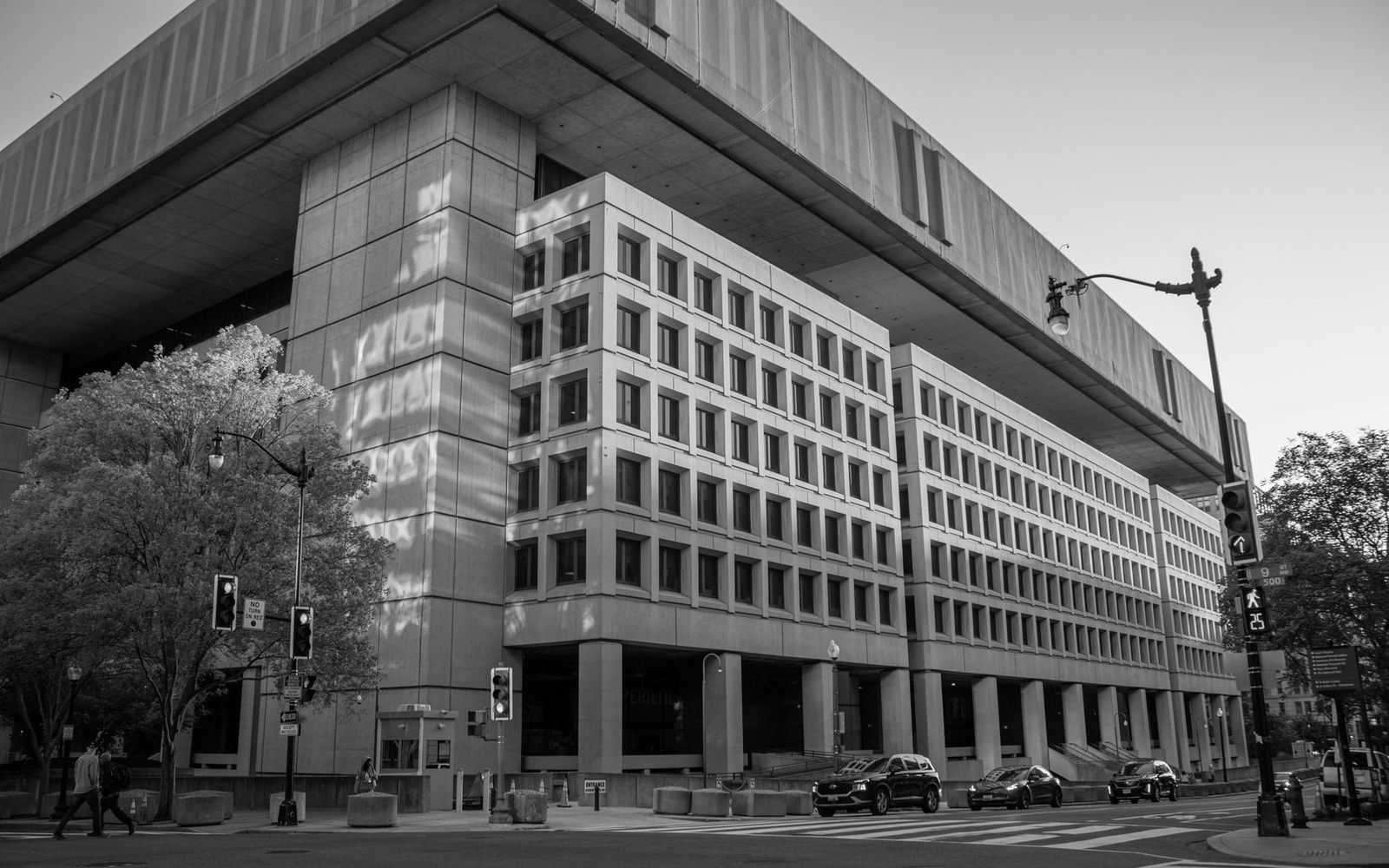 Cantilevered concrete office building overhangs a street corner lined with parked cars