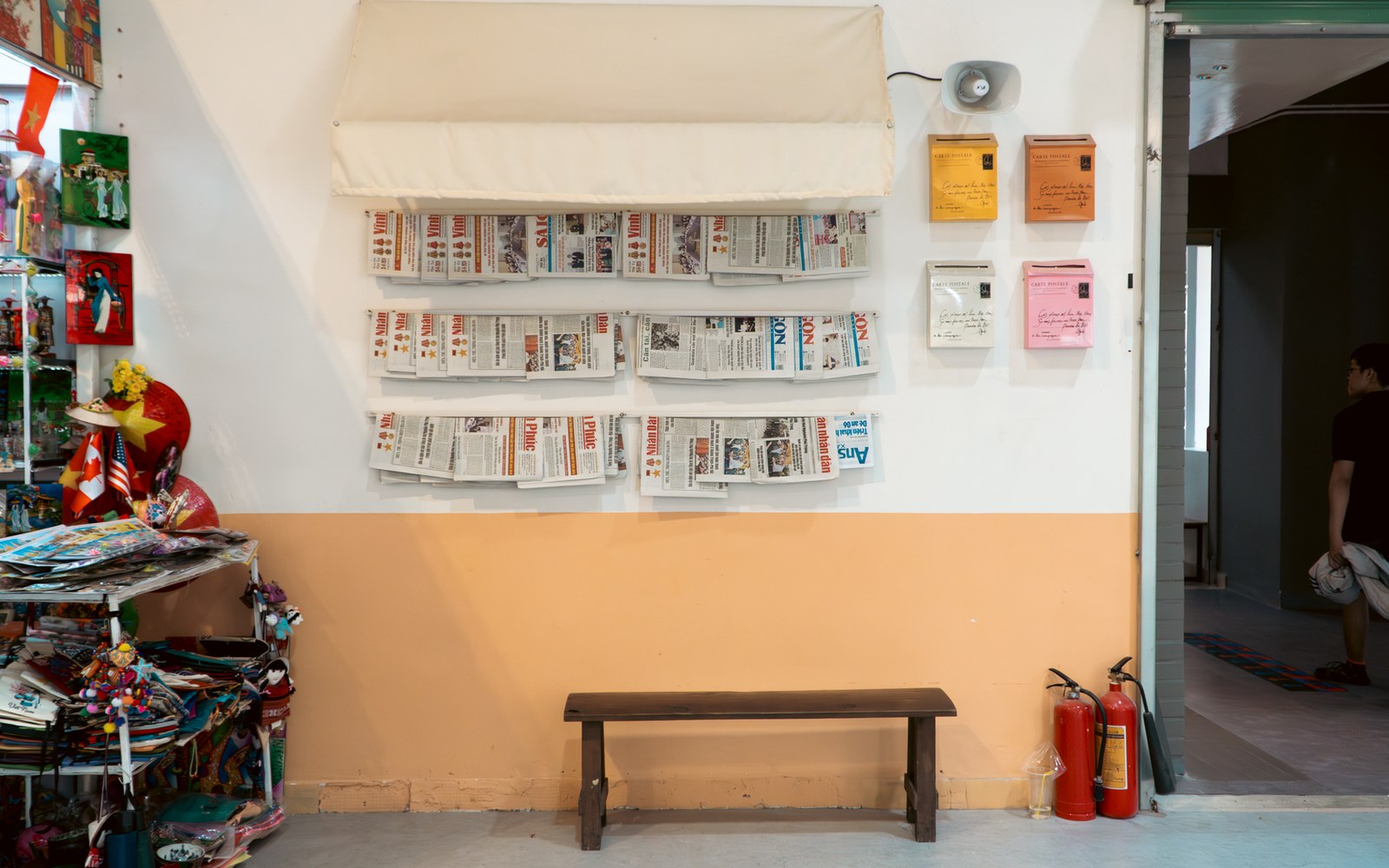 Newspapers displayed in wall racks beside a wooden bench and fire extinguishers