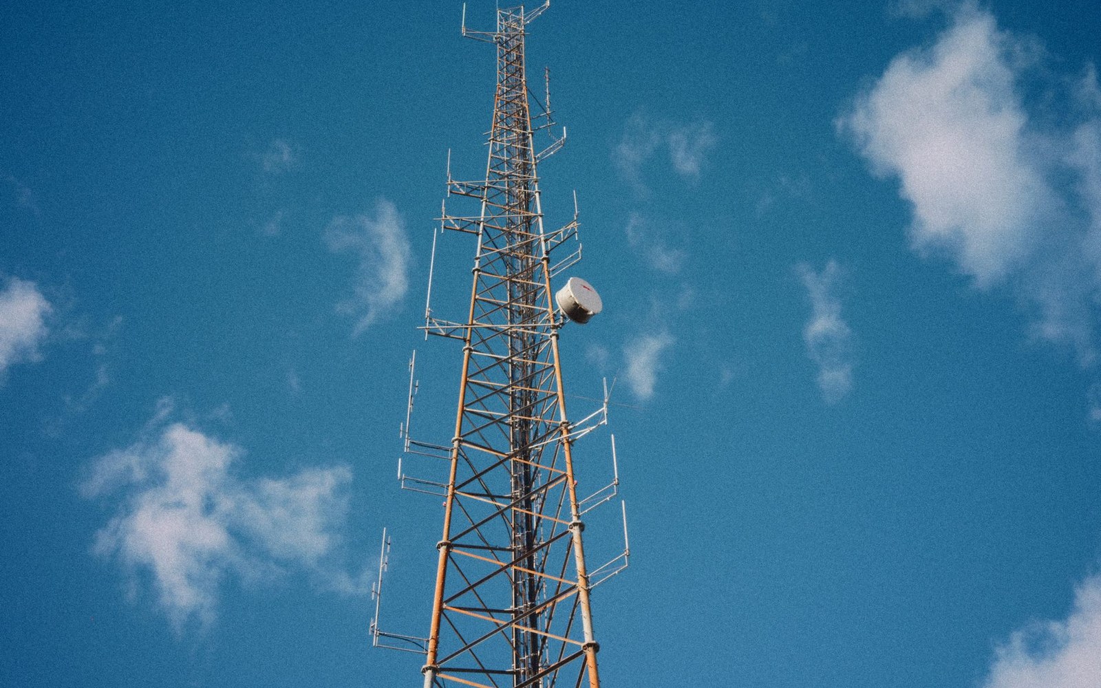 Tall telecommunications tower with antennas and a satellite dish against a blue sky