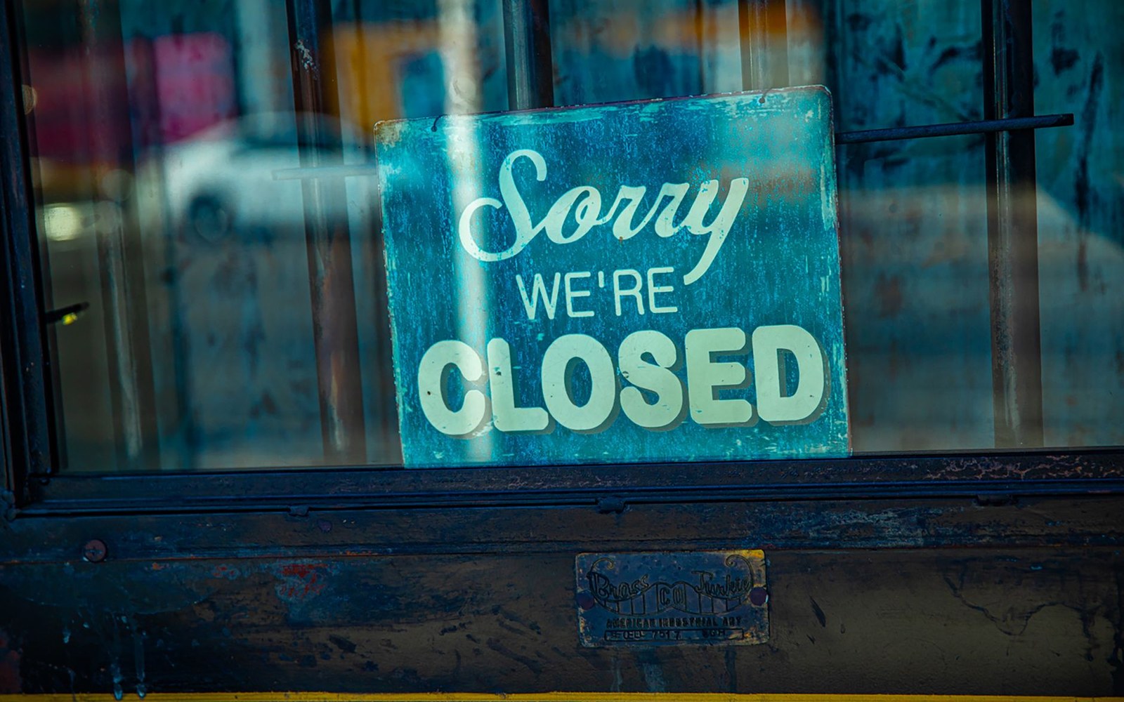 The locked glass-front entrance of a closed small-city newspaper office, the masthead still mounted above the door, a notice taped inside