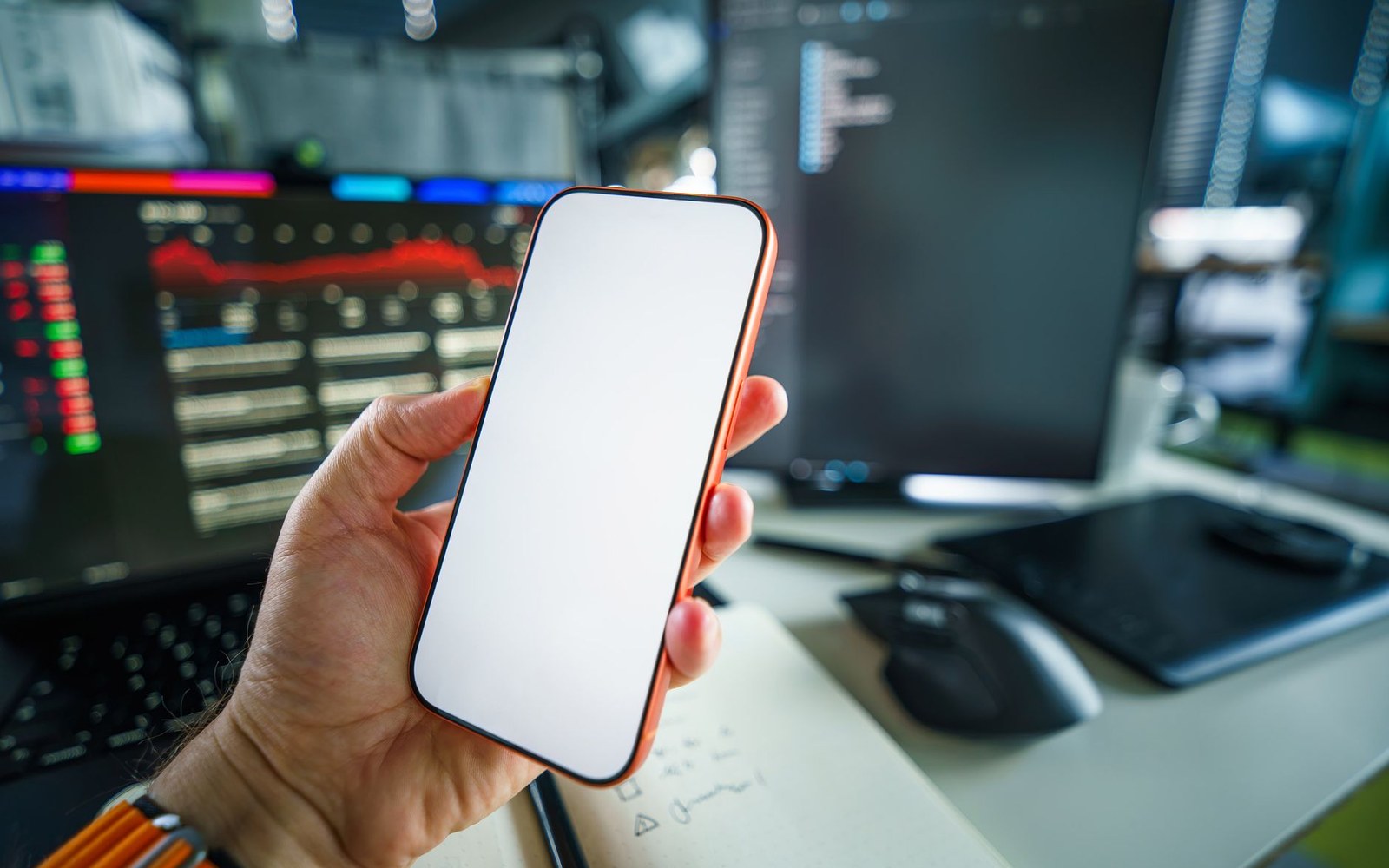 An adult hand holding a phone showing a streaming service home screen, a printed Nielsen chart visible on the desk surface below